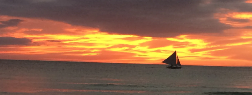 Sunset over White Beach, a paraw sailboat on the horizon