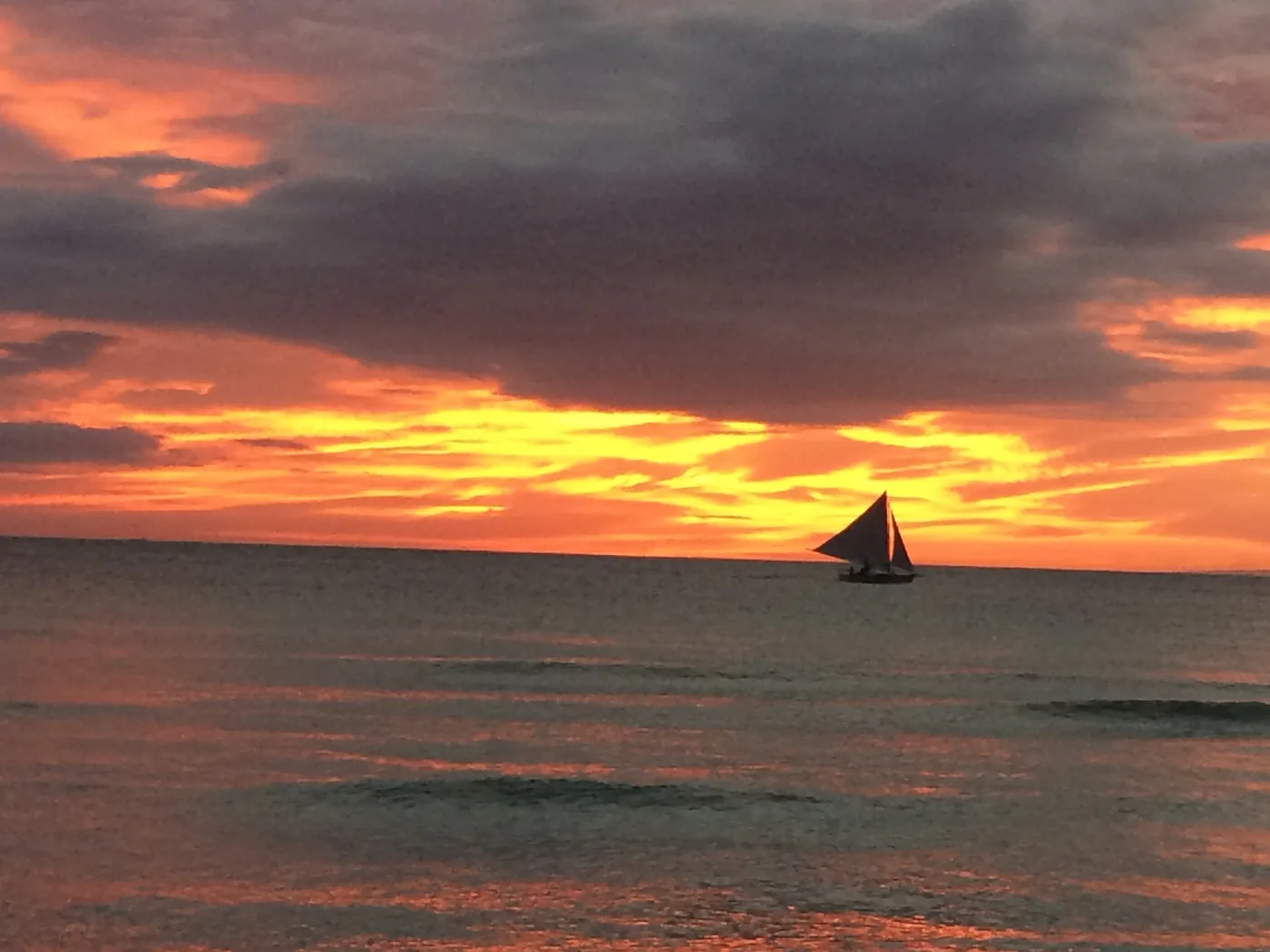 Sunset over White Beach, a paraw sailboat on the horizon