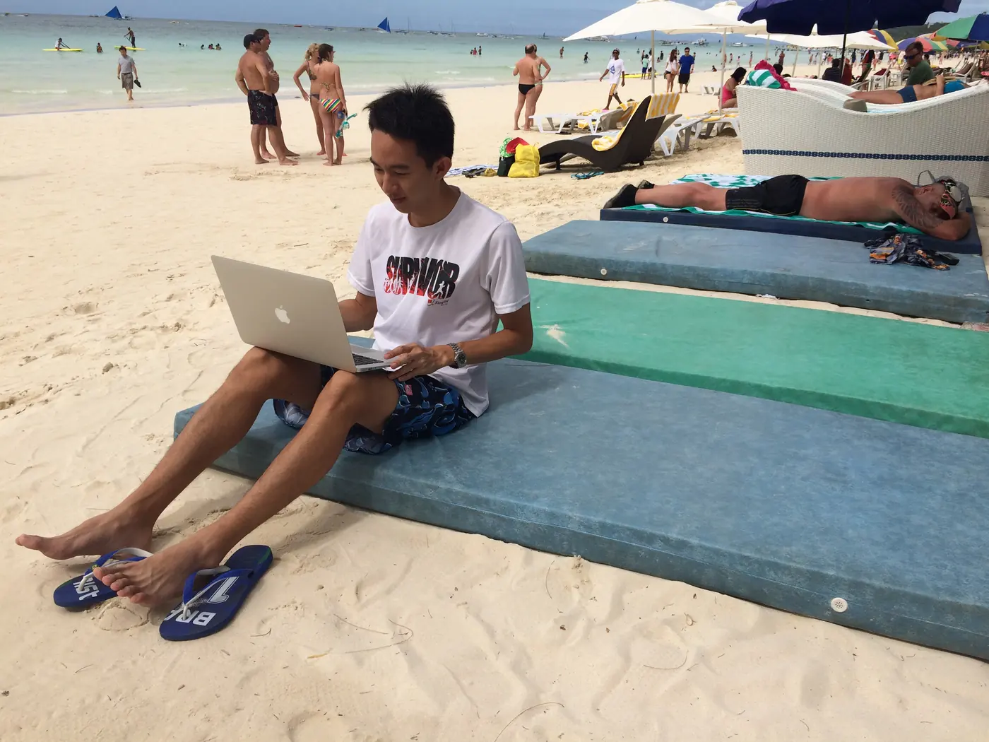 Working on a laptop on a beach mat, White Beach behind