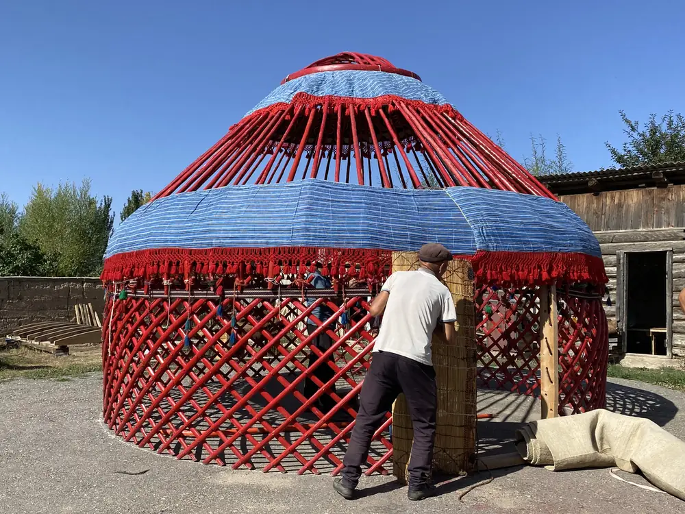 A craftsman fitting felt onto a red and blue yurt frame