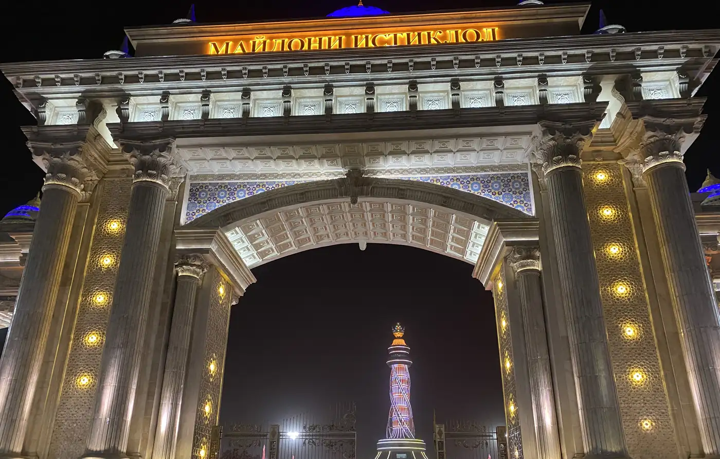 A lit arch at night framing the flagpole tower in Dushanbe