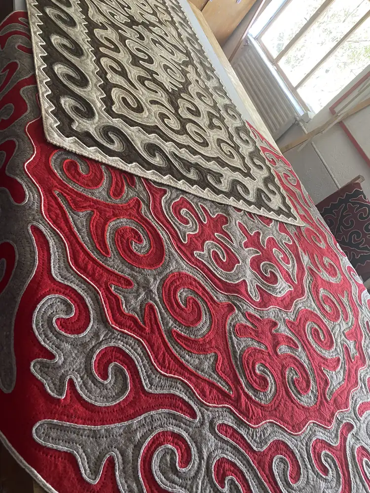 A red and grey shyrdak felt carpet at a yurt workshop