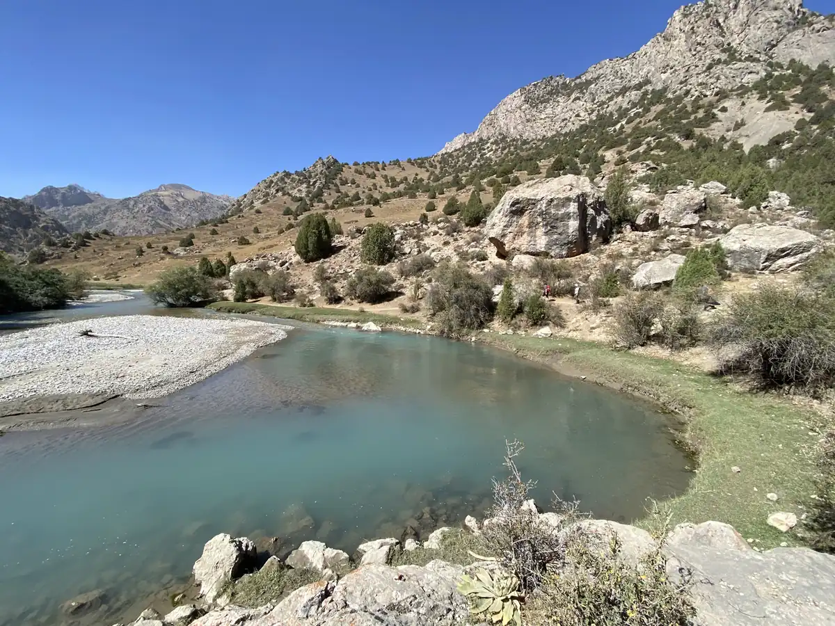 A clear turquoise river winding through a wide valley in the Fann Mountains