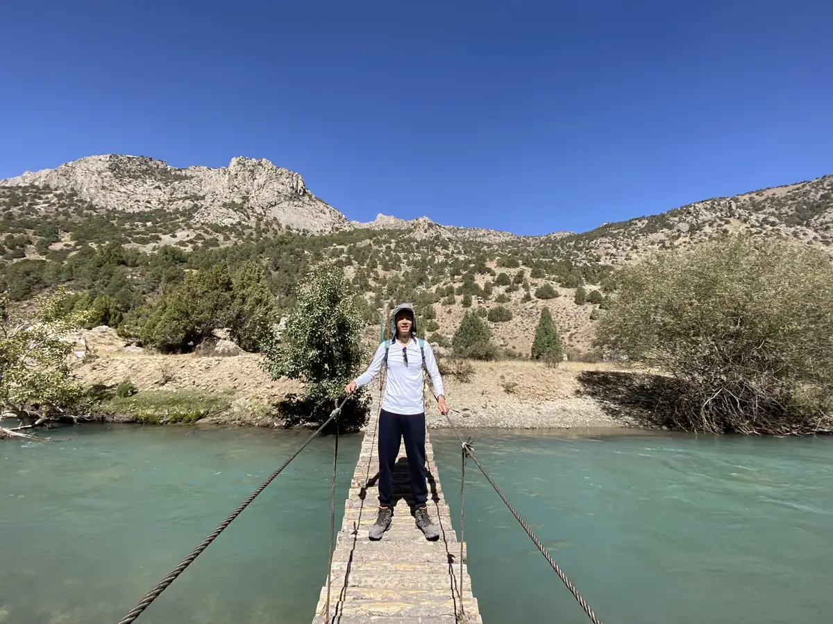 Spencer Li on a wooden footbridge over a turquoise river near Sarytag