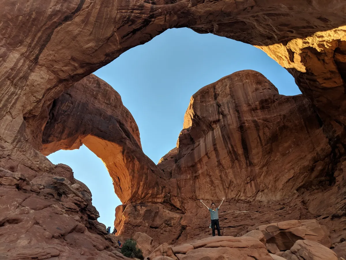 Spencer, arms up, under a huge red rock arch in Arches National Park