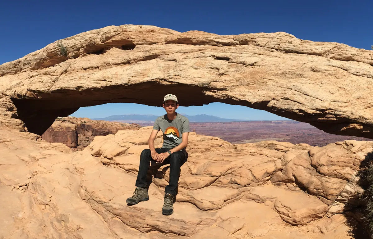 Spencer sitting under a rock arch on the canyon rim in Canyonlands