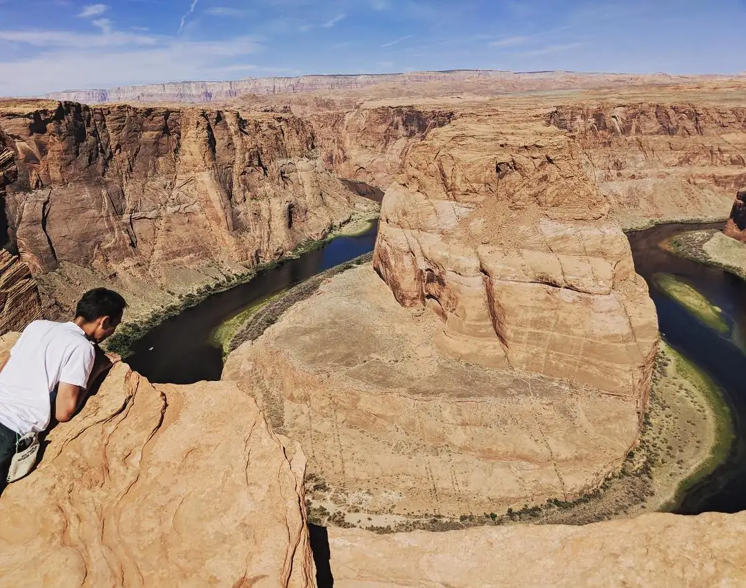 Spencer leaning out over Horseshoe Bend, with the Colorado River looping below